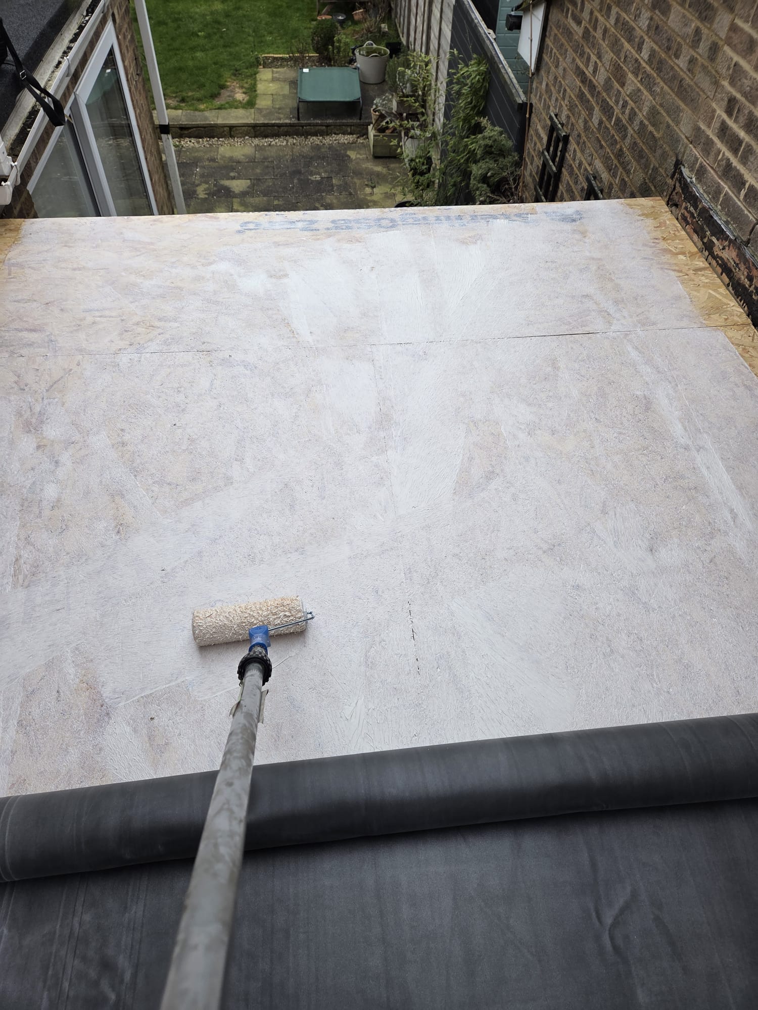 Flat roof deck primed during EPDM roofing preparation with roller visible