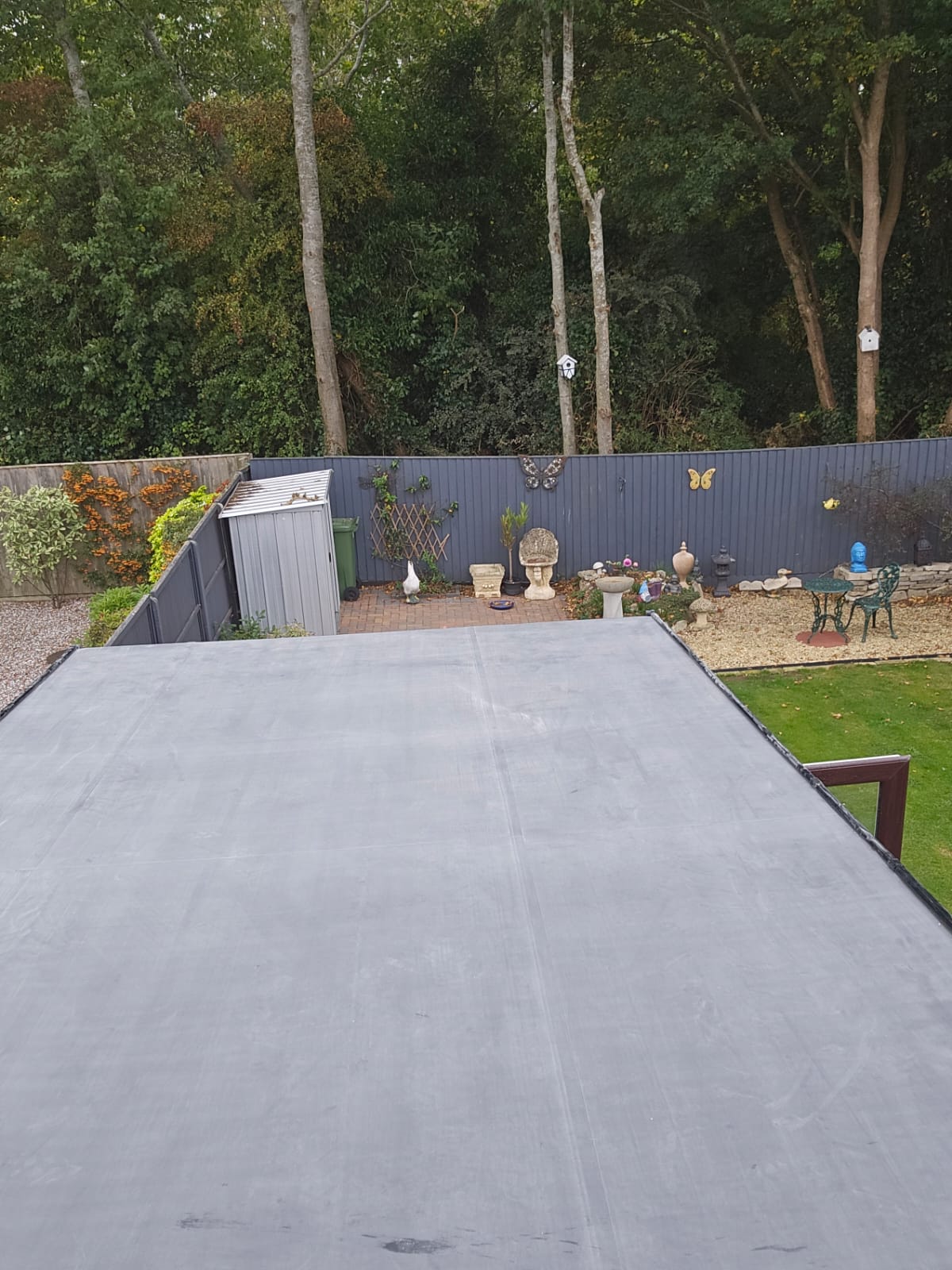 Completed EPDM flat roof in a back garden setting with mature trees and fencing